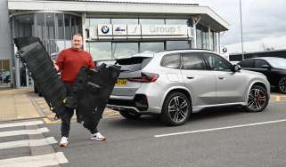 Auto Express news reporter Ellis Hyde holding two BMW iX1 undertrays